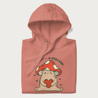 Folded light pink hoodie with a graphic of a mushroom character holding a heart and the text 'There's Mushroom in My Heart for You'.