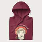 Folded maroon hoodie with a graphic of a cute mushroom character holding a flower and the text 'You're a real fun-gal!'.