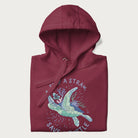 Folded maroon hoodie with a graphic of a sea turtle with coral on it's shell and the text 'Skip a Straw, Save a Turtle'.