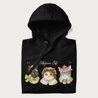 Folded black hoodie with a graphic of three cats in vintage-inspired attire and the text 'Cottagecore Cats'.