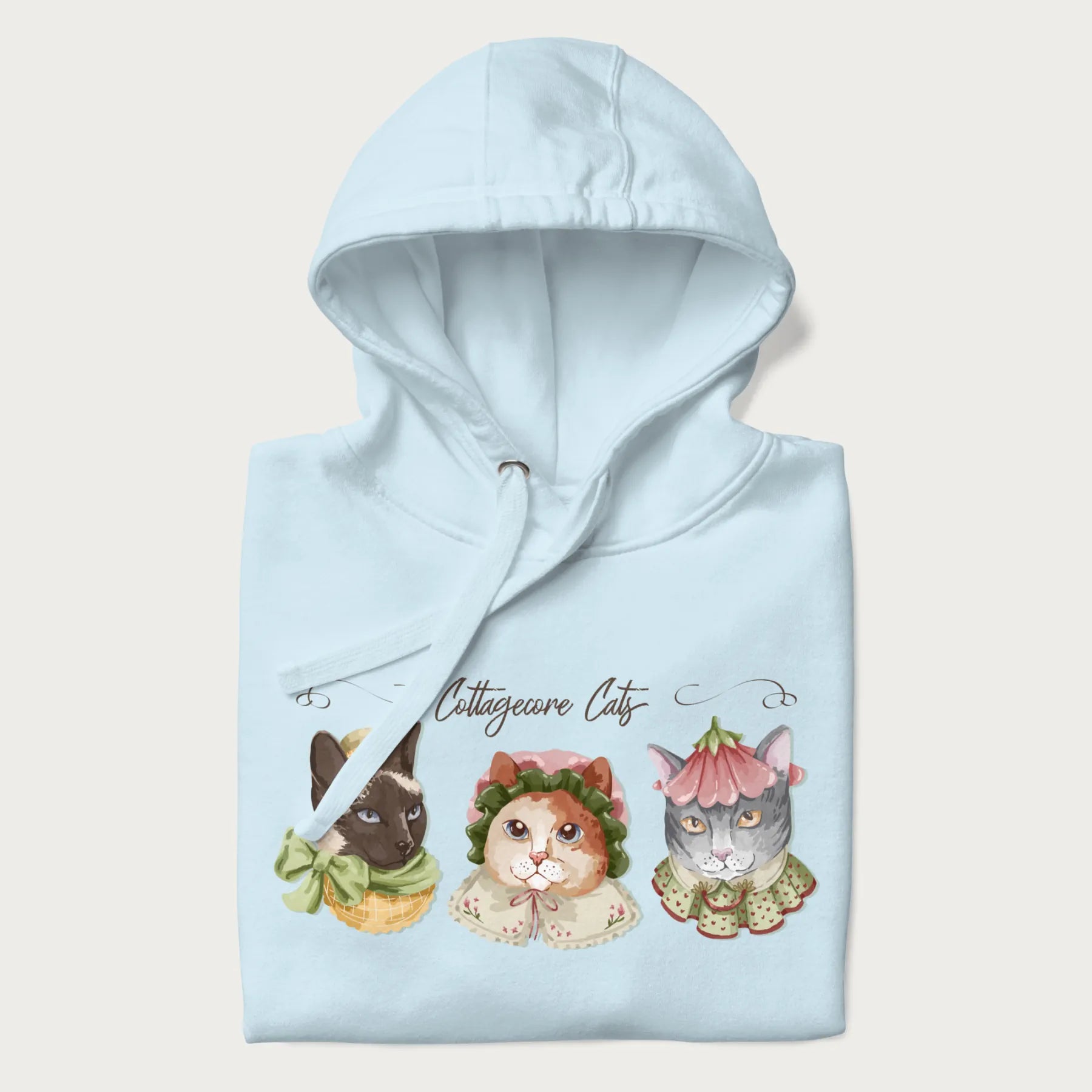 Folded light blue hoodie with a graphic of three cats in vintage-inspired attire and the text 'Cottagecore Cats'.