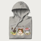 Folded light grey hoodie with a graphic of three cats in vintage-inspired attire and the text 'Cottagecore Cats'.