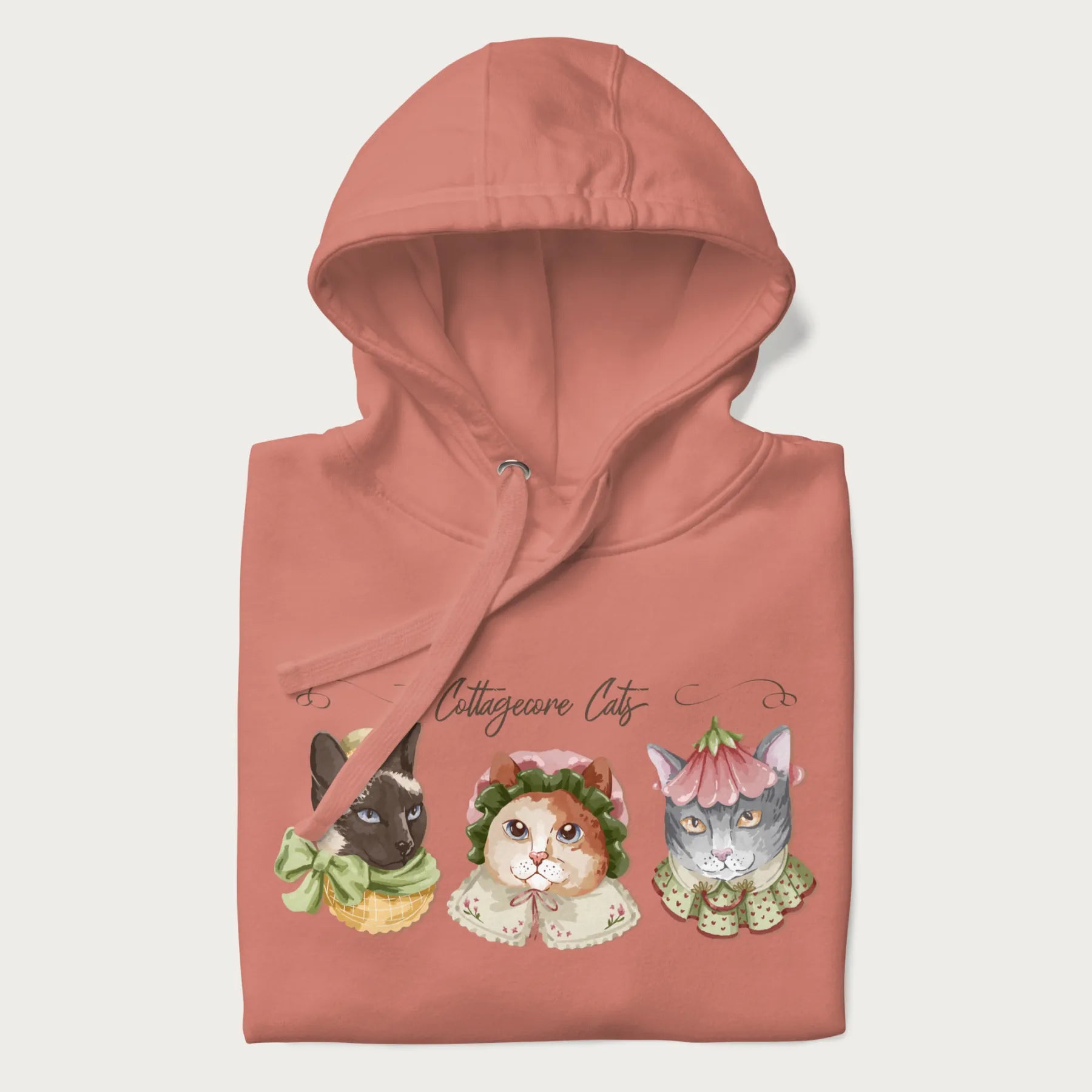 Folded light pink hoodie with a graphic of three cats in vintage-inspired attire and the text 'Cottagecore Cats'.