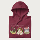 Folded maroon hoodie with a graphic of three cats in vintage-inspired attire and the text 'Cottagecore Cats'.