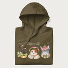 Folded military green hoodie with a graphic of three cats in vintage-inspired attire and the text 'Cottagecore Cats'.