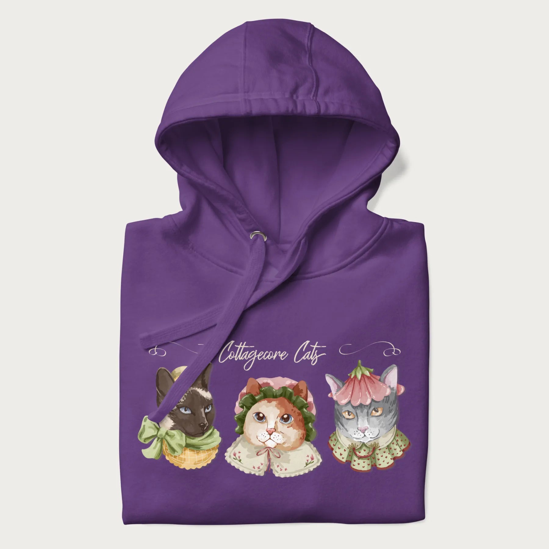 Folded purple hoodie with a graphic of three cats in vintage-inspired attire and the text 'Cottagecore Cats'.