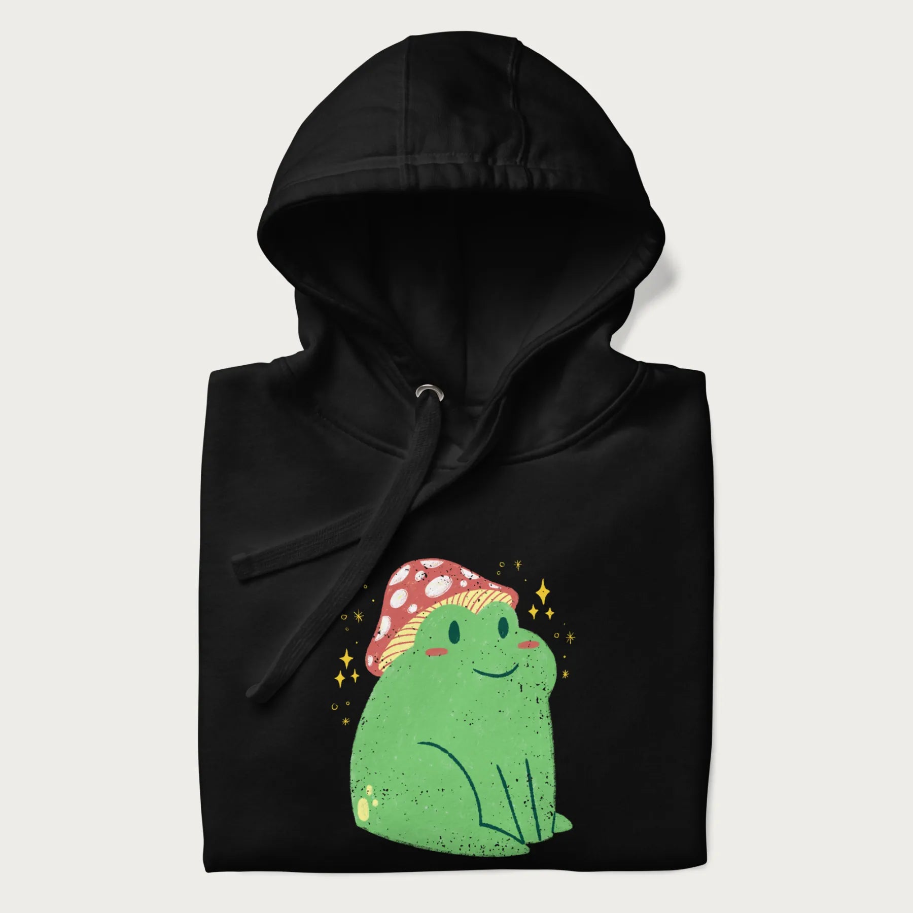 Folded black hoodie with a graphic of a green frog wearing a mushroom cap surrounded by stars.