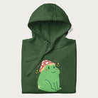 Folded forest green hoodie with a graphic of a green frog wearing a mushroom cap surrounded by stars.