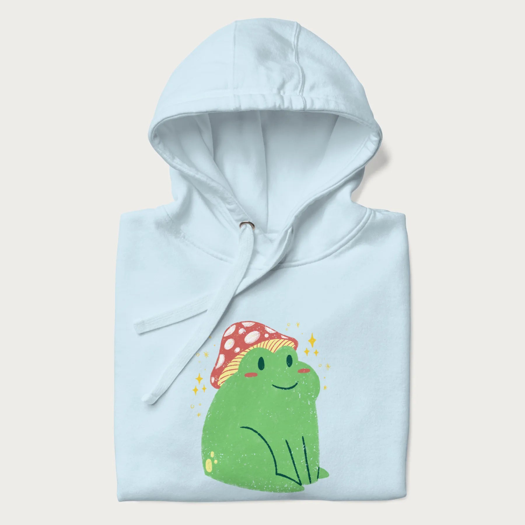 Folded light blue hoodie with a graphic of a green frog wearing a mushroom cap surrounded by stars.