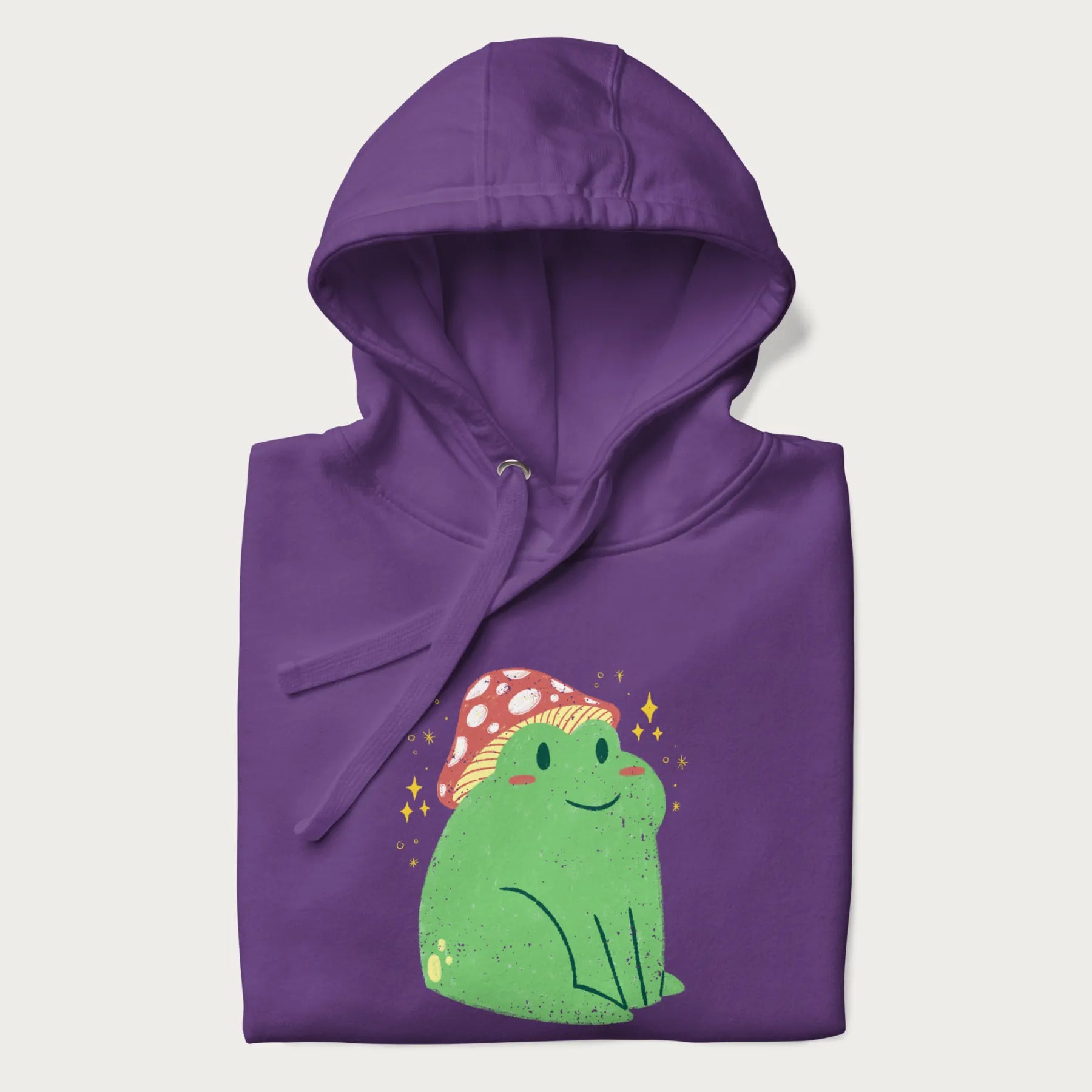Folded purple hoodie with a graphic of a green frog wearing a mushroom cap surrounded by stars.