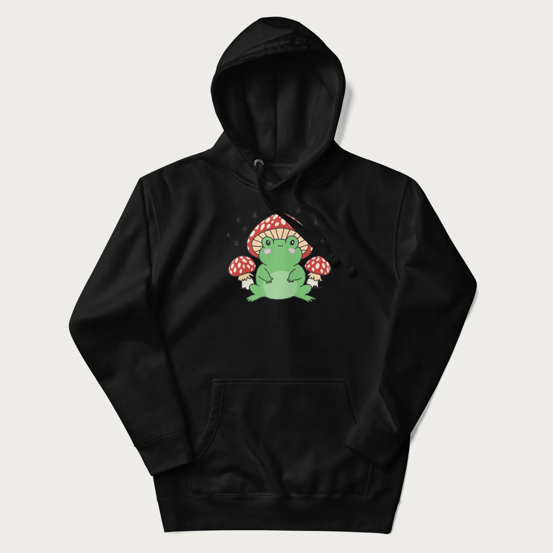 Folded black hoodie will illustration of a cute green frog with red and white mushrooms.