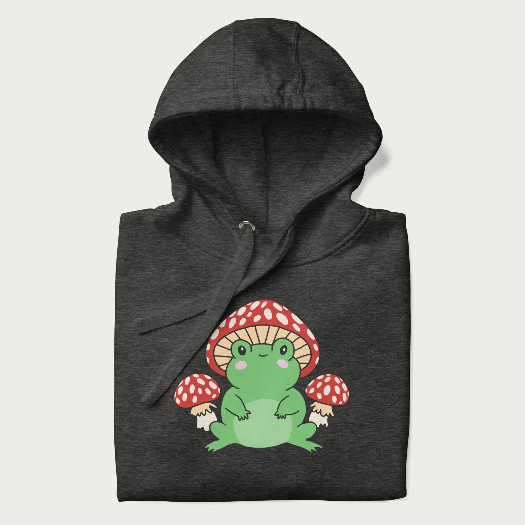 Folded dark grey hoodie will illustration of a cute green frog with red and white mushrooms.