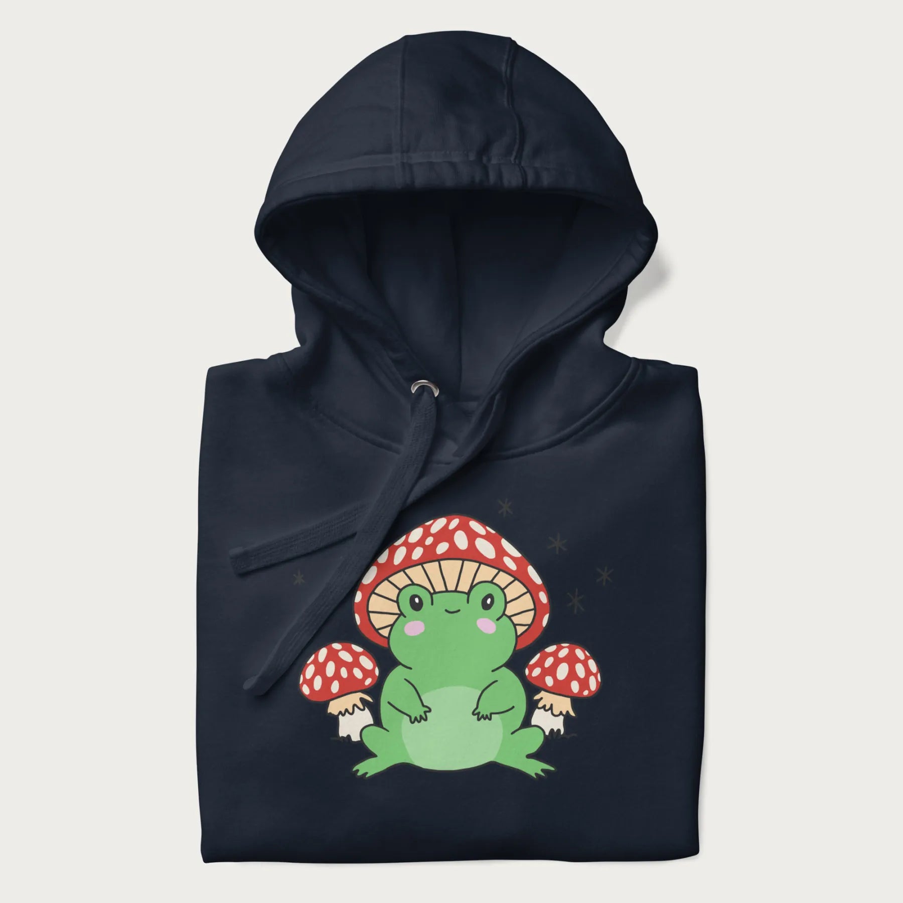 Folded navy blue hoodie will illustration of a cute green frog with red and white mushrooms.