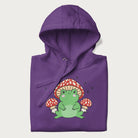 Folded purple hoodie will illustration of a cute green frog with red and white mushrooms.