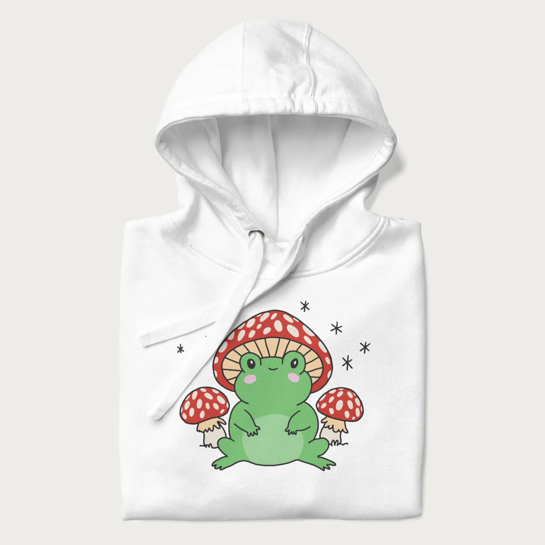 Folded white hoodie will illustration of a cute green frog with red and white mushrooms.