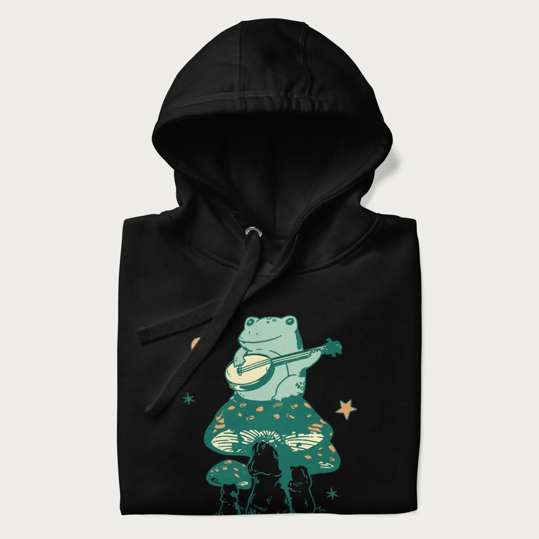 Folded black hoodie with graphic of a frog playing a banjo on a mushroom with stars and a crescent moon.