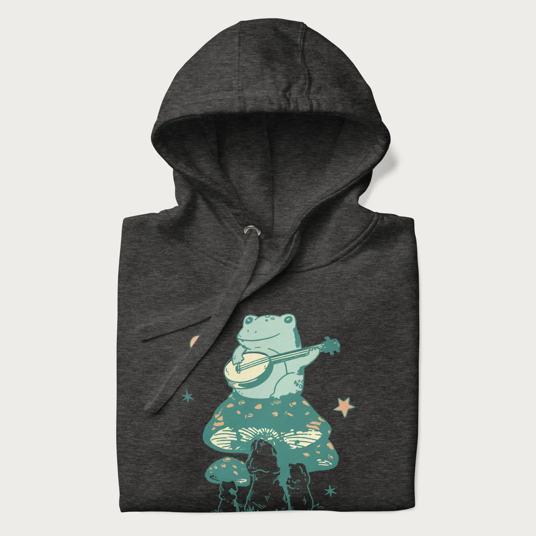 Folded dark grey hoodie with graphic of a frog playing a banjo on a mushroom with stars and a crescent moon.