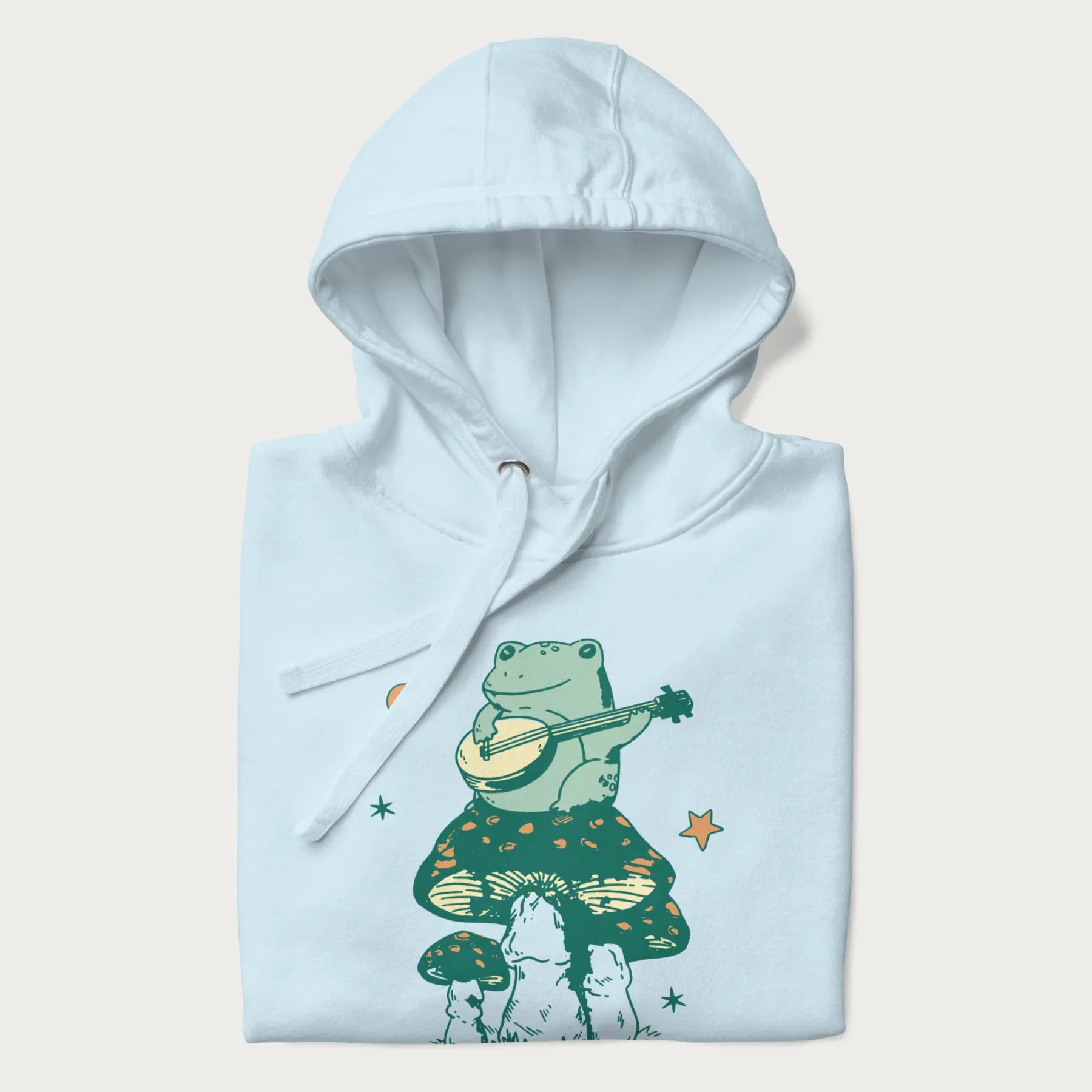 Folded light blue hoodie with graphic of a frog playing a banjo on a mushroom with stars and a crescent moon.