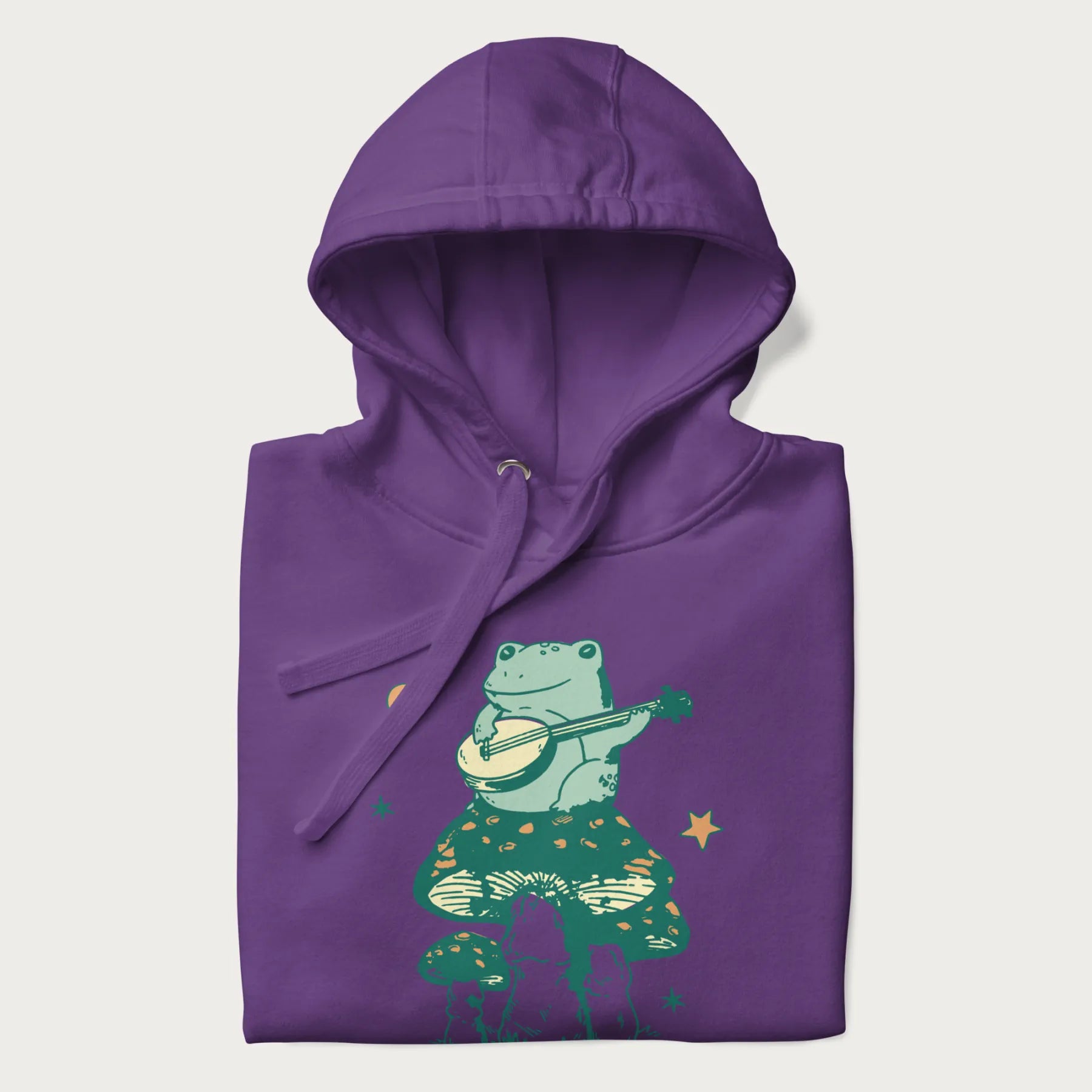 Folded purple hoodie with graphic of a frog playing a banjo on a mushroom with stars and a crescent moon.