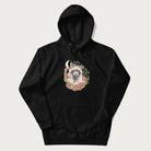 Black hoodie with graphic of an adorable raccoon surrounded by mushrooms, foliage, and a crescent moon with stars in the background.