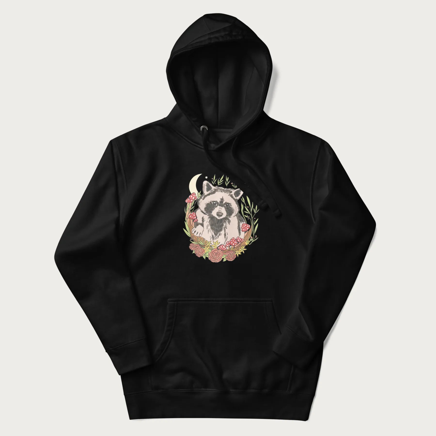 Black hoodie with graphic of an adorable raccoon surrounded by mushrooms, foliage, and a crescent moon with stars in the background.