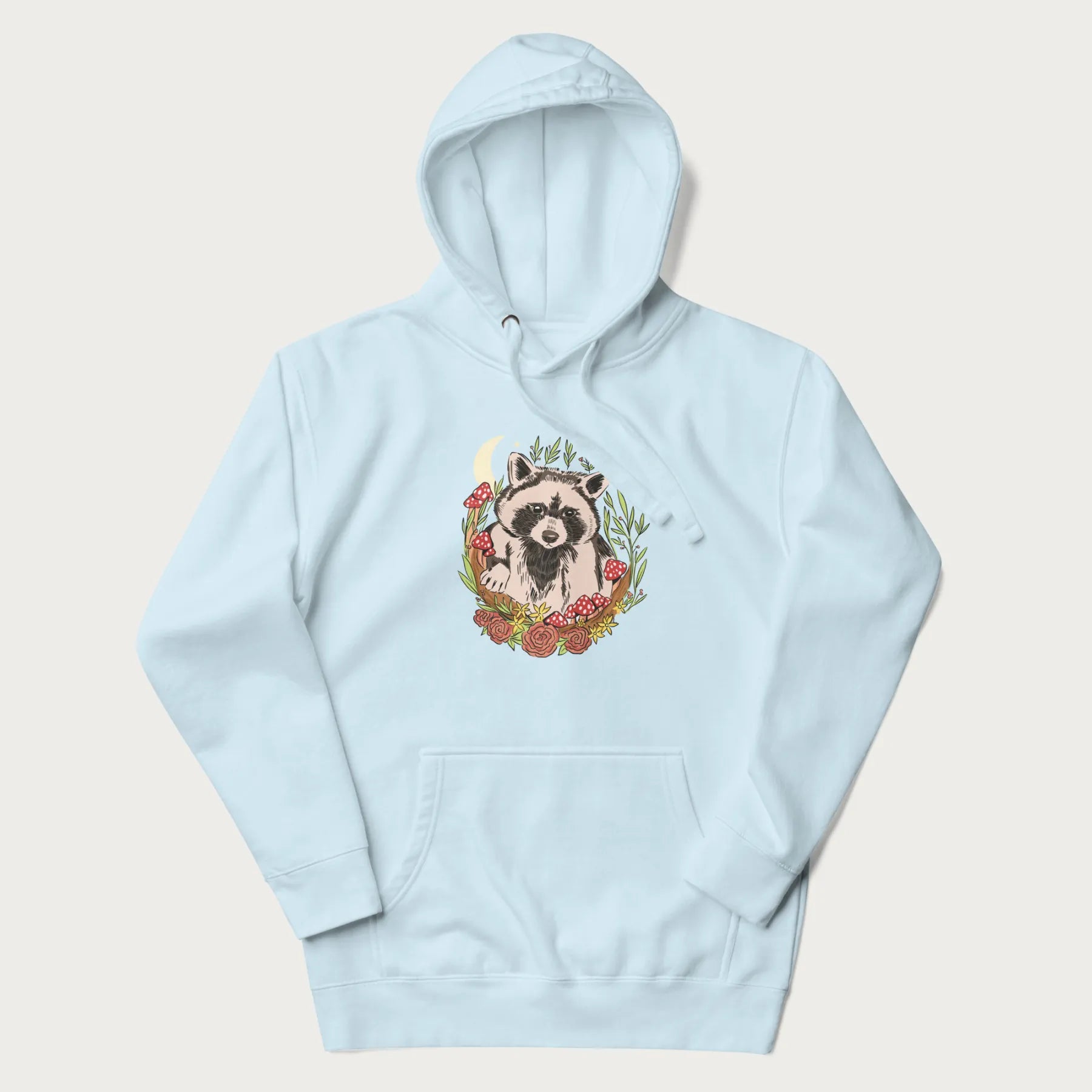 Light blue hoodie with graphic of an adorable raccoon surrounded by mushrooms, foliage, and a crescent moon with stars in the background.