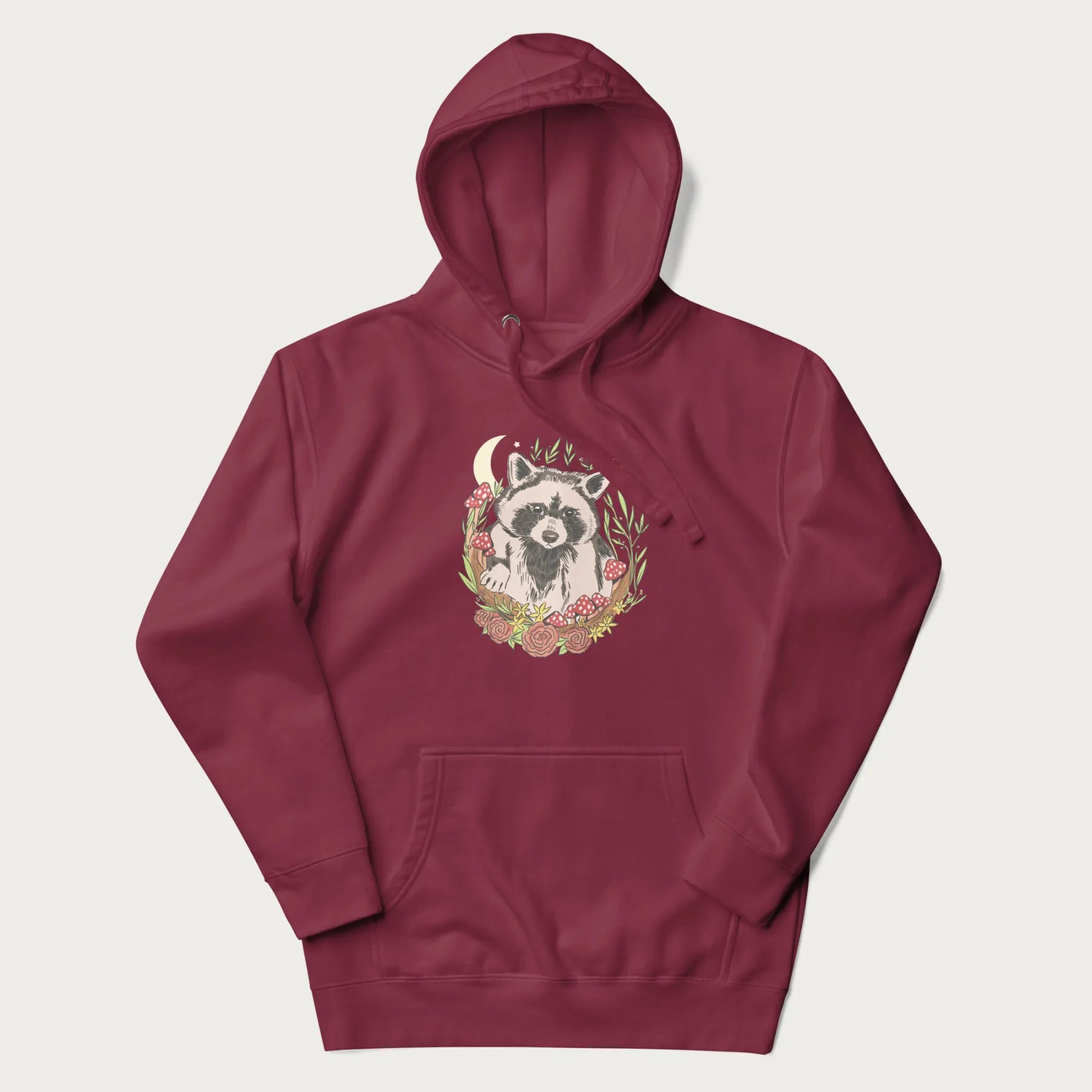 Maroon hoodie with graphic of an adorable raccoon surrounded by mushrooms, foliage, and a crescent moon with stars in the background.