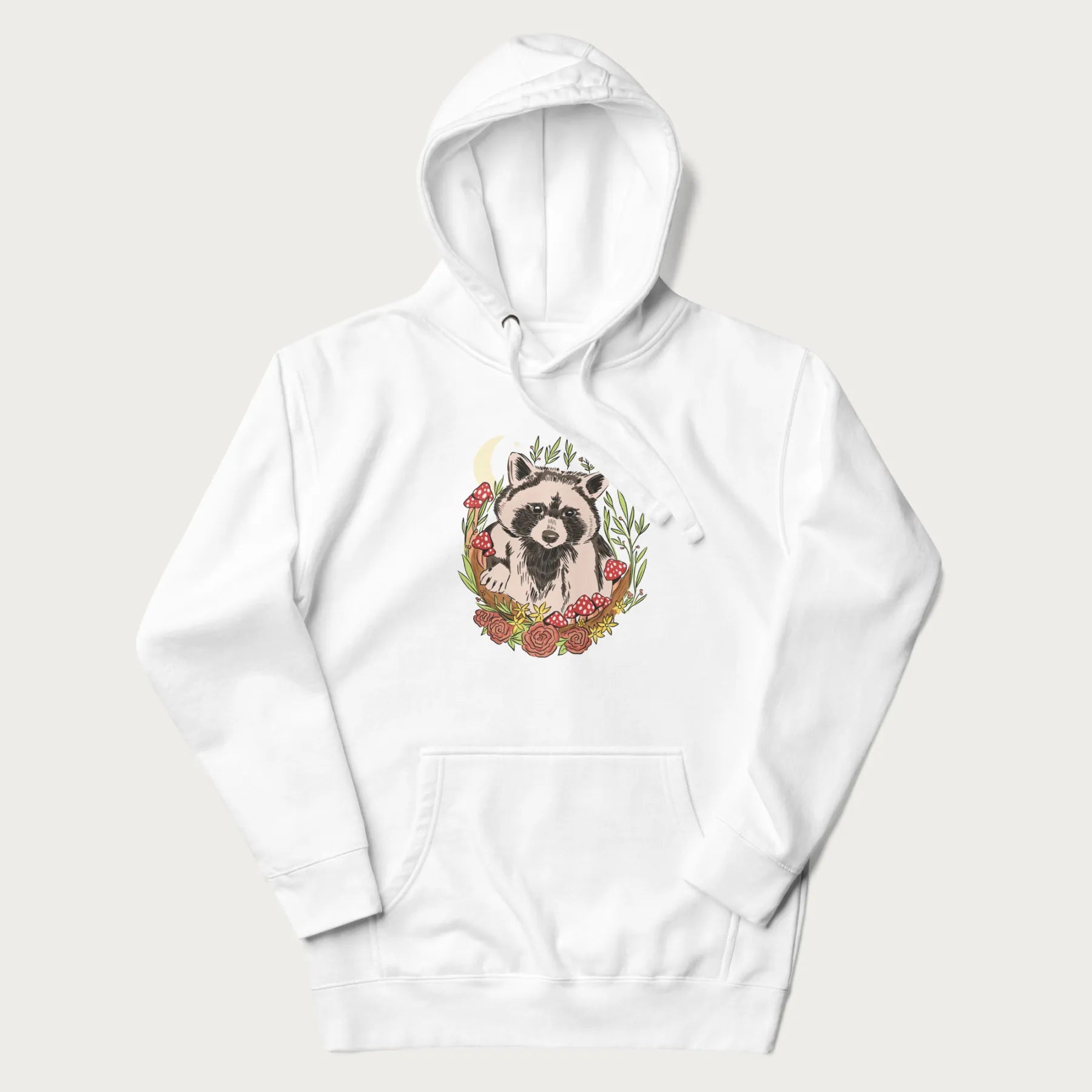 White hoodie with graphic of an adorable raccoon surrounded by mushrooms, foliage, and a crescent moon with stars in the background.