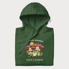 Folded forest green hoodie with a graphic of a frog lounging under mushrooms and the phrases 'Don't Be Stressin' Life's a Blessing'.
