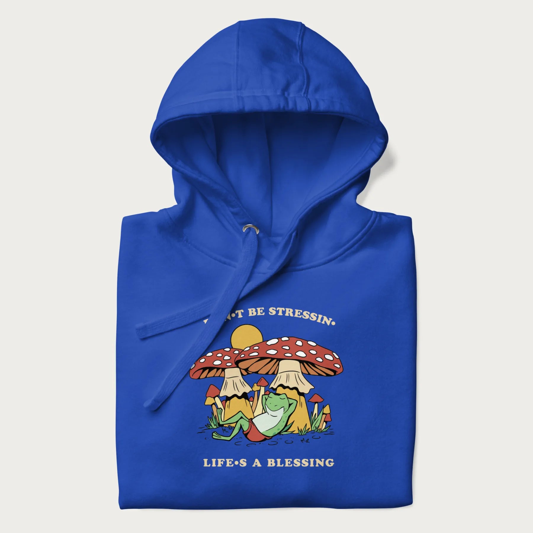 Folded royal blue hoodie with a graphic of a frog lounging under mushrooms and the phrases 'Don't Be Stressin' Life's a Blessing'.