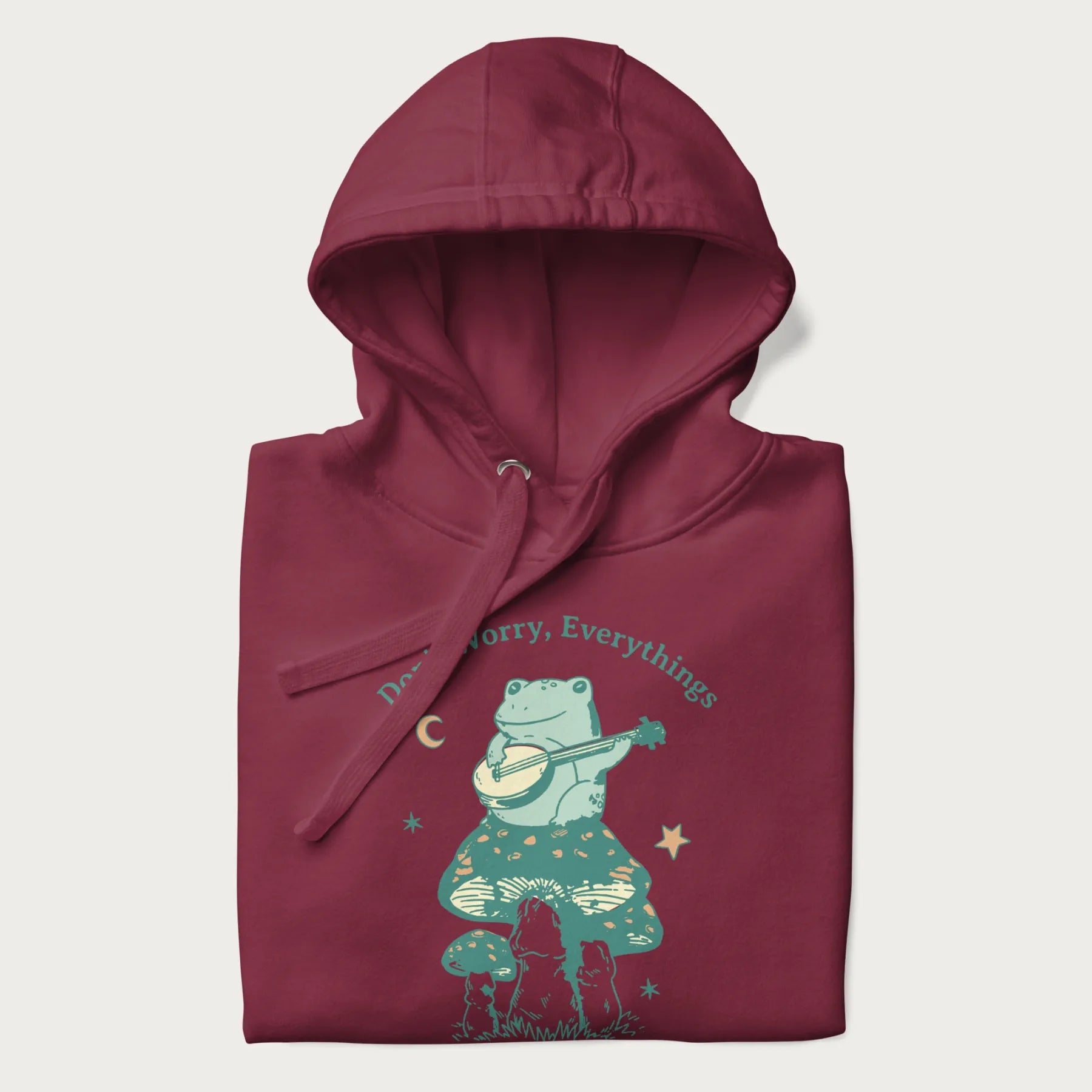 Folded maroon hoodie with a graphic of a frog playing a banjo on a mushroom under the moon and stars, with the text 'Don't Worry, Everything's Gonna Be Just Fine.'