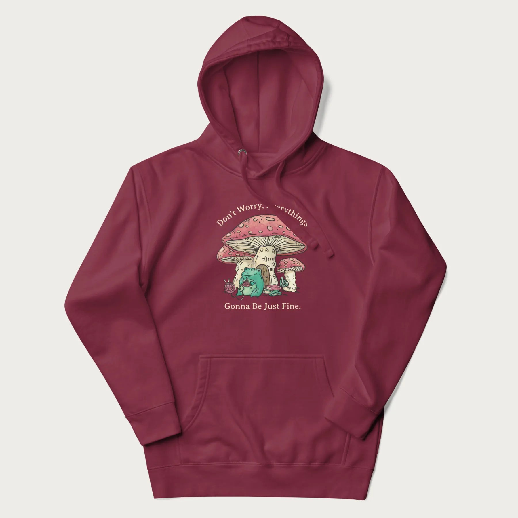 Maroon hoodie with a graphic of a frog knitting under a large mushroom with the text 'Don't Worry, Everything's Gonna Be Just Fine'.