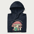 Folded navy blue hoodie with a graphic of a frog knitting under a large mushroom with the text 'Don't Worry, Everything's Gonna Be Just Fine'.