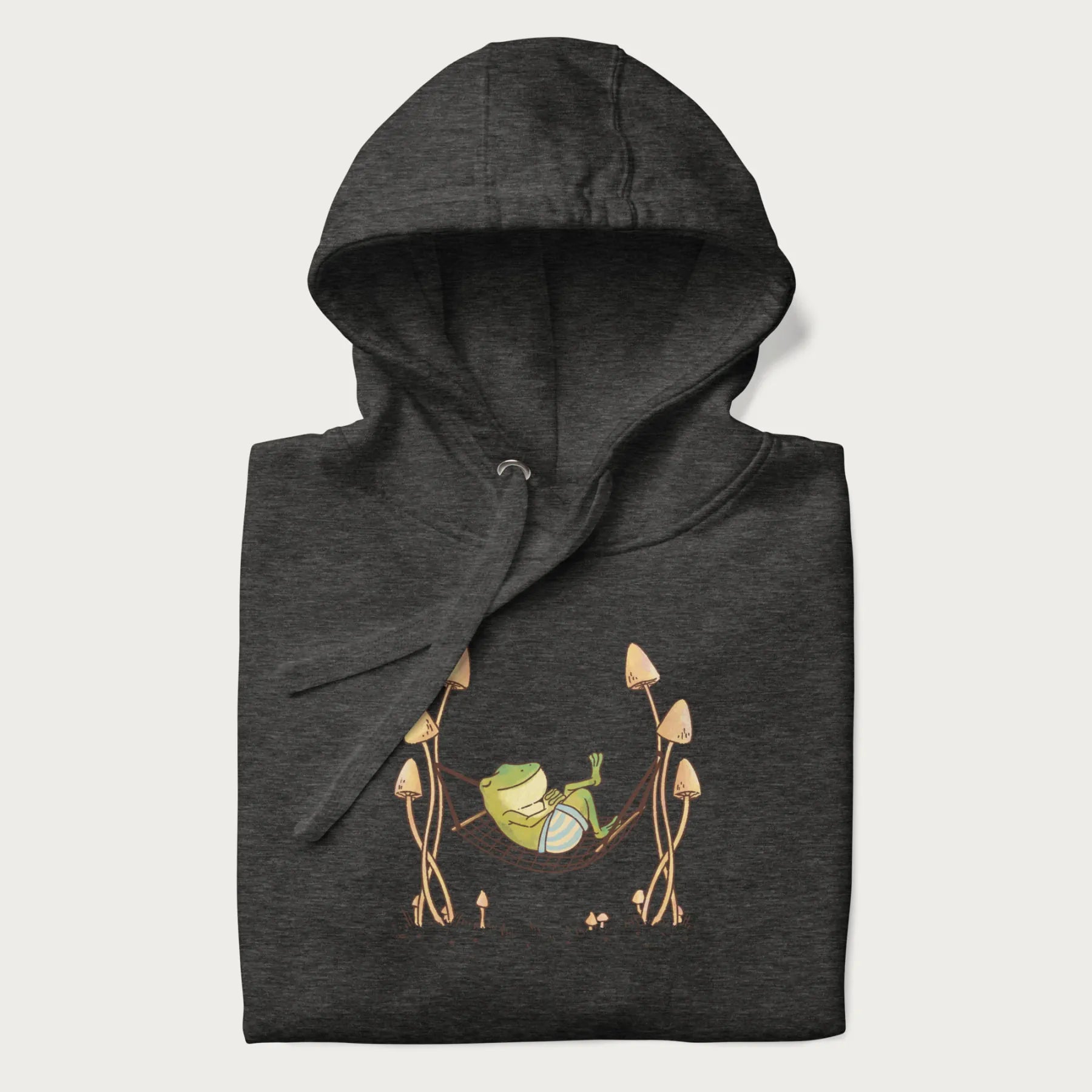 Folded dark grey hoodie with a graphic of a frog lounging in a hammock between tall mushrooms.