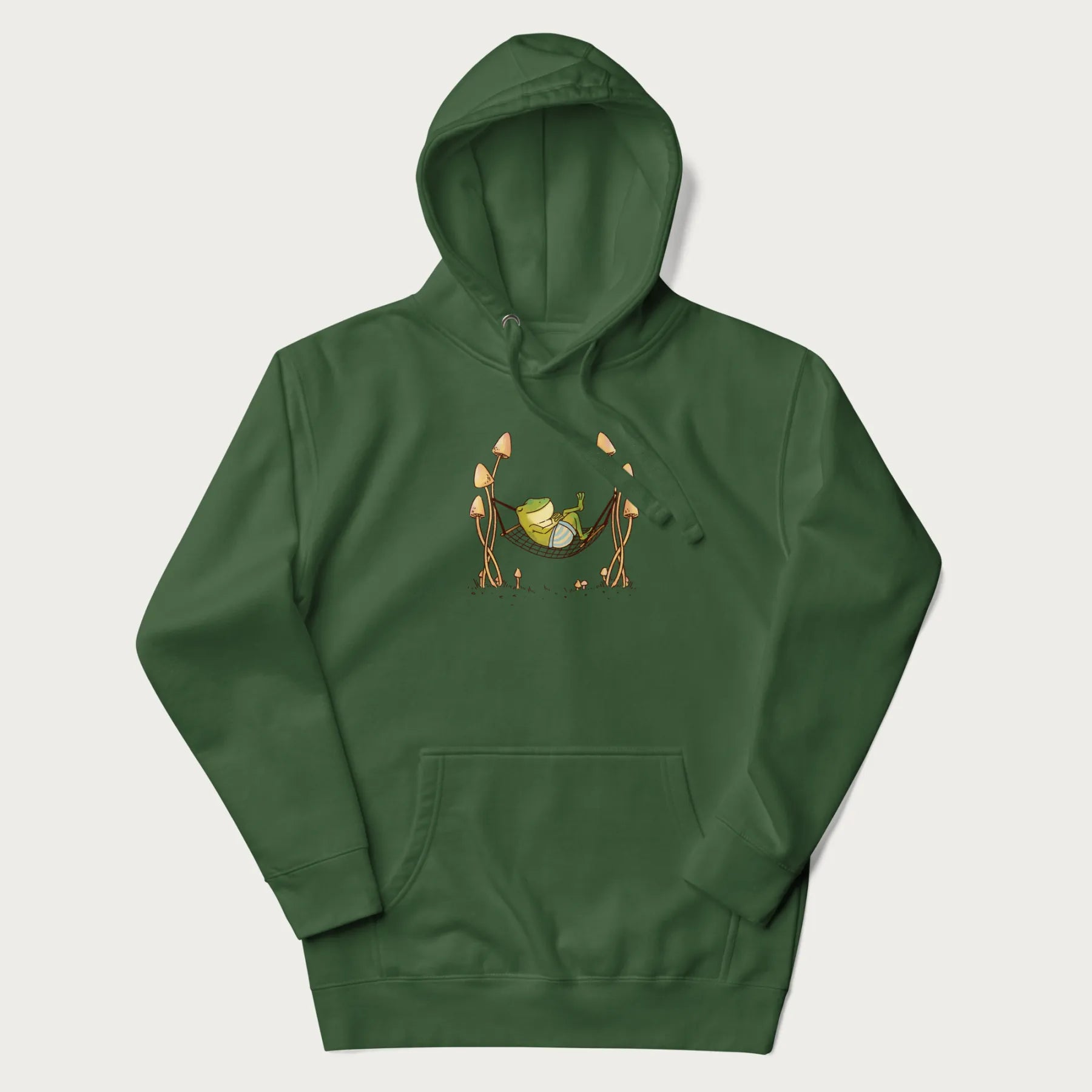 Forest green hoodie with a graphic of a frog lounging in a hammock between tall mushrooms.