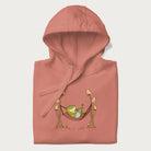 Folded light pink hoodie with a graphic of a frog lounging in a hammock between tall mushrooms.