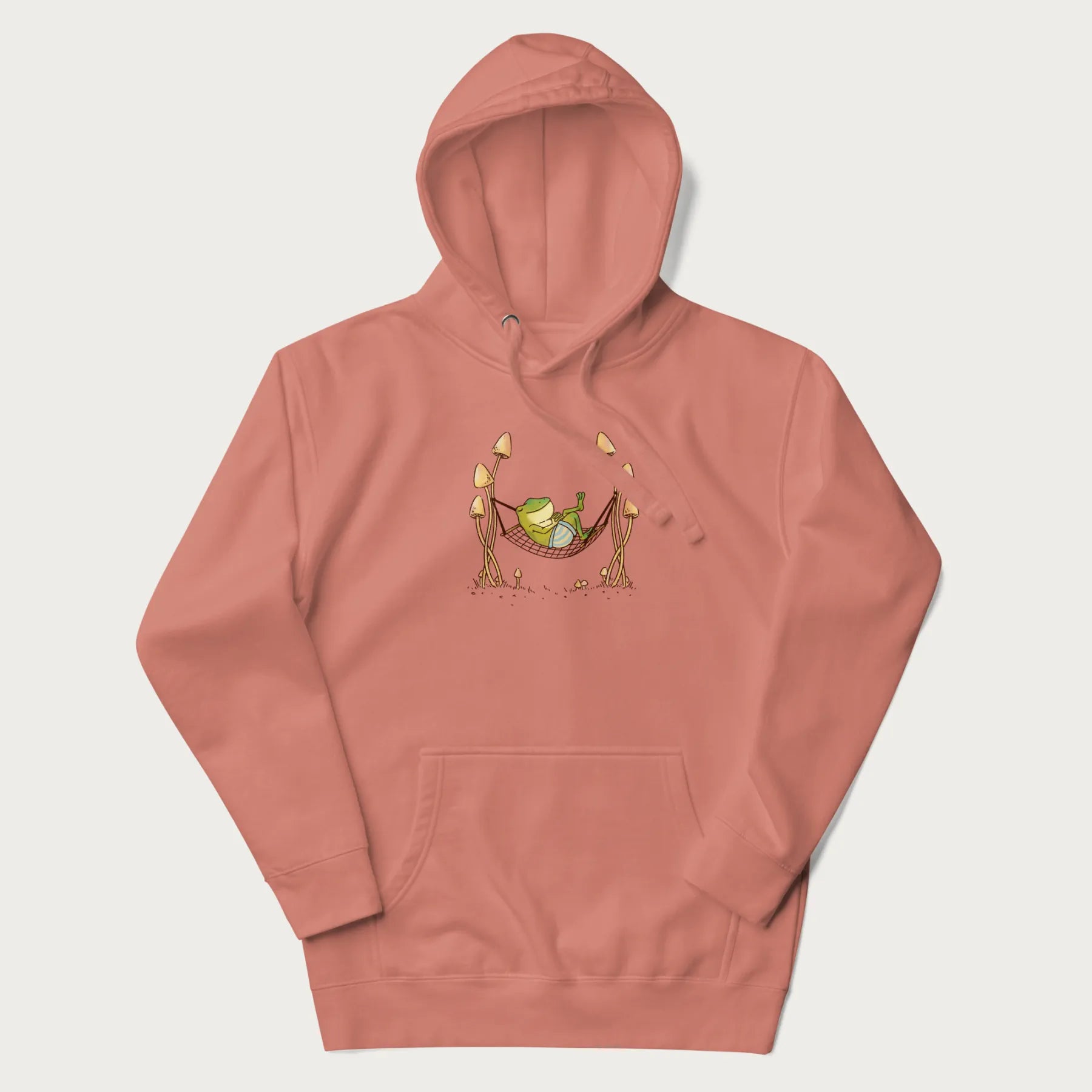 Light pink hoodie with a graphic of a frog lounging in a hammock between tall mushrooms.