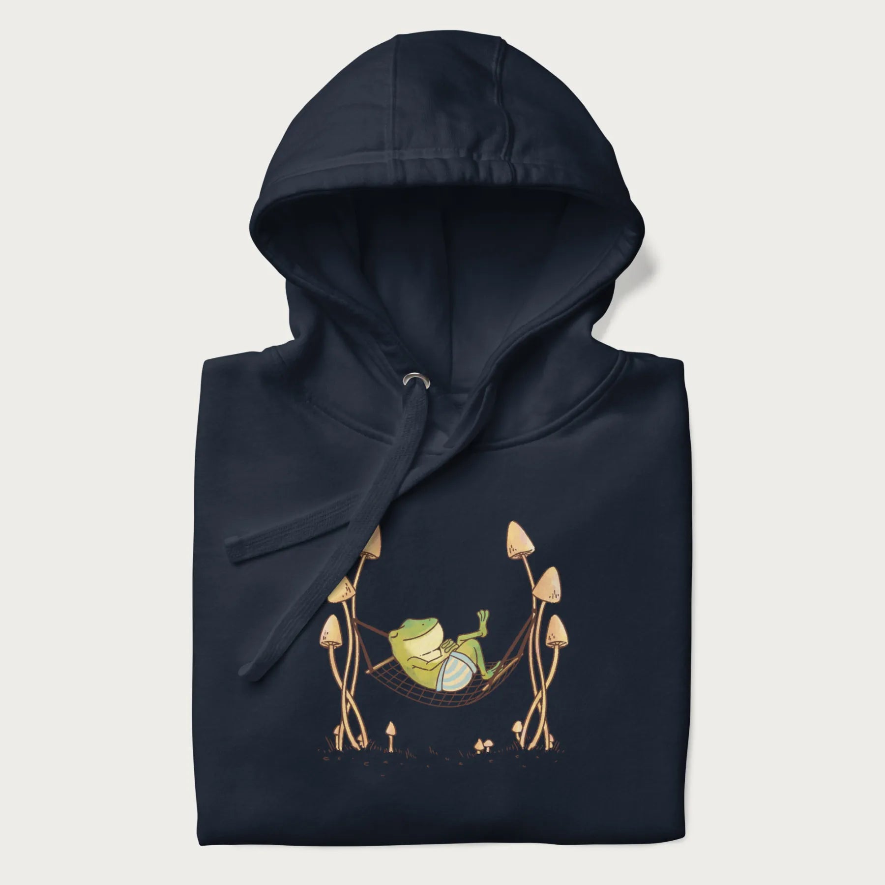 Folded navy blue hoodie with a graphic of a frog lounging in a hammock between tall mushrooms.