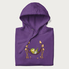 Folded purple hoodie with a graphic of a frog lounging in a hammock between tall mushrooms.
