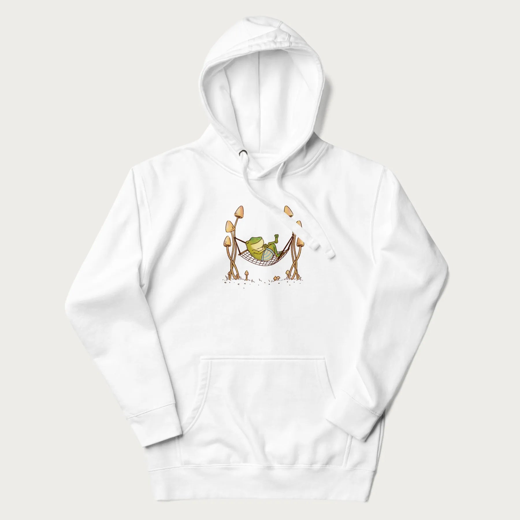 White hoodie with a graphic of a frog lounging in a hammock between two tall mushrooms.