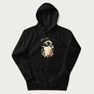 Black hoodie with a graphic of a cat nestled among flowers and mushrooms with the text 'Home is Where My Cat Is' above.