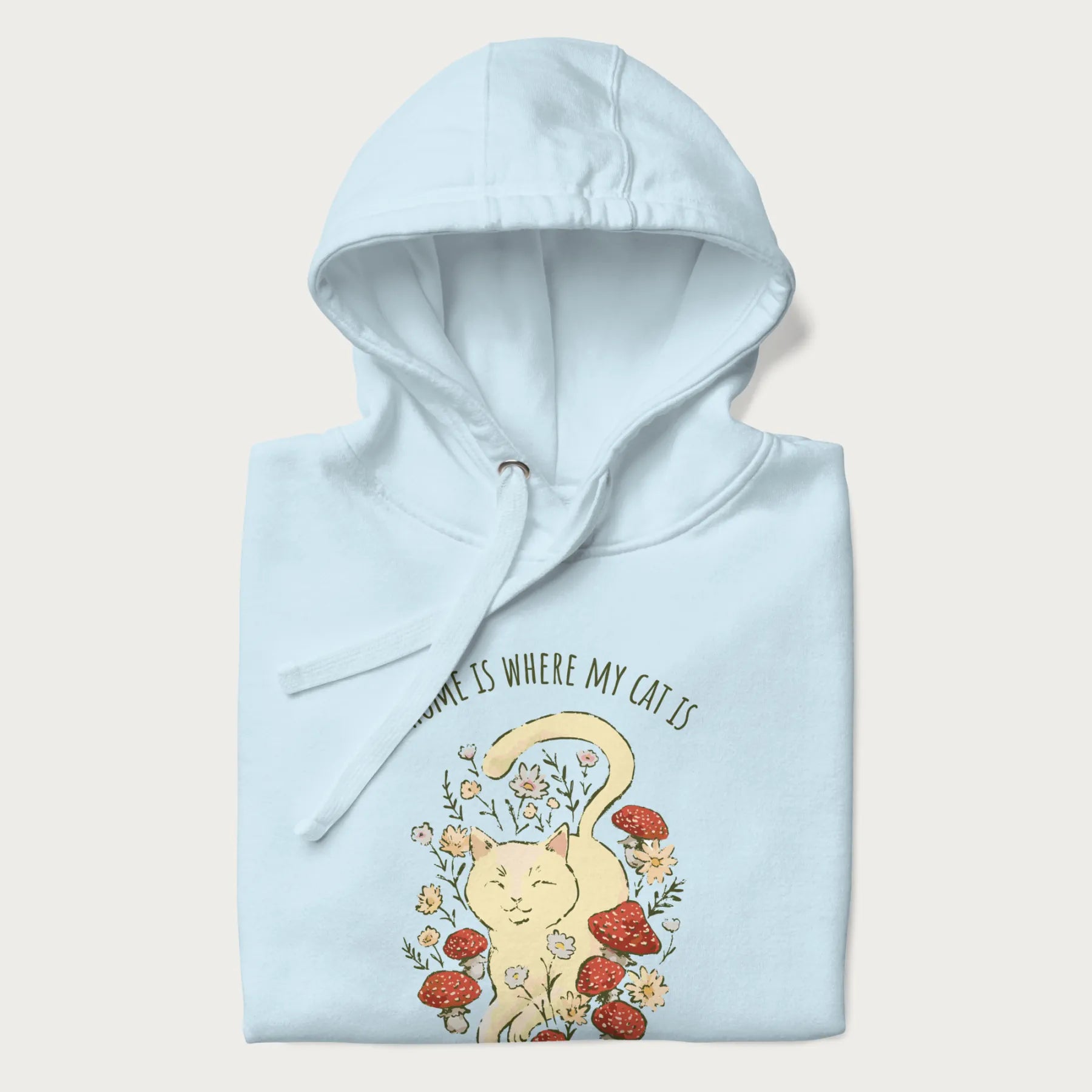 Folded light blue hoodie with a graphic of a cat nestled among flowers and mushrooms with the text 'Home is Where My Cat Is' above.