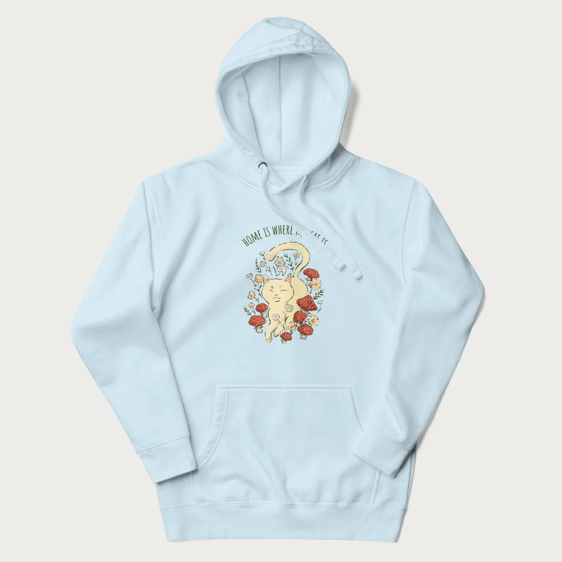 Light blue hoodie with a graphic of a cat nestled among flowers and mushrooms with the text 'Home is Where My Cat Is' above.