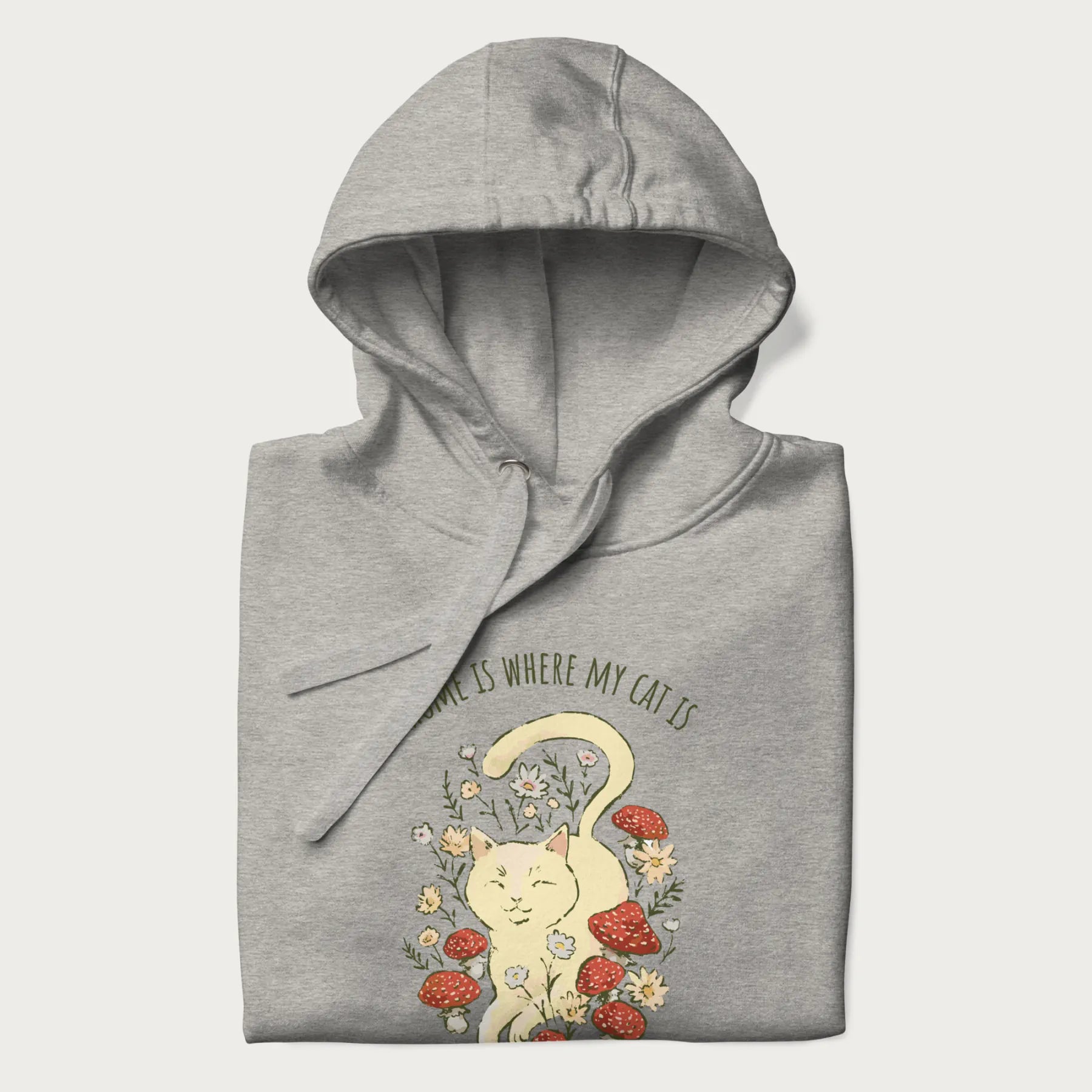Folded light grey hoodie with a graphic of a cat nestled among flowers and mushrooms with the text 'Home is Where My Cat Is' above.