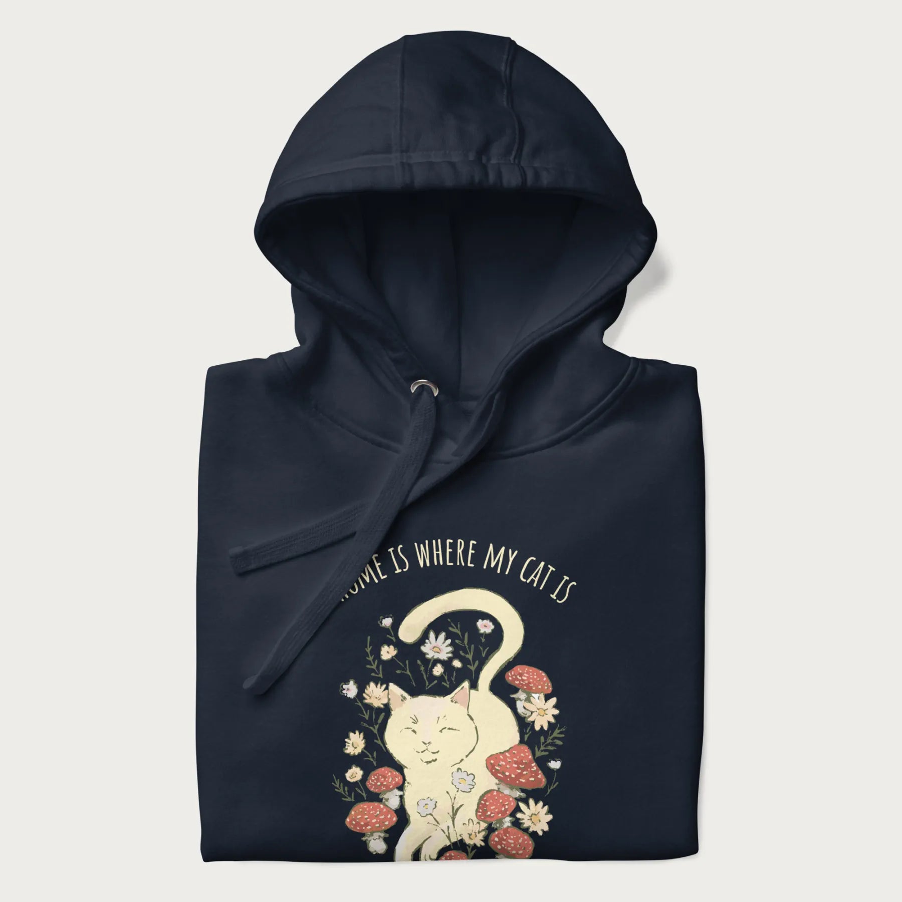 Folded navy blue hoodie with a graphic of a cat nestled among flowers and mushrooms with the text 'Home is Where My Cat Is' above.