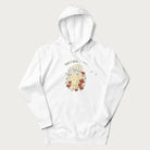 White hoodie with a graphic of a cat nestled among flowers and mushrooms with the text 'Home is Where My Cat Is' above.