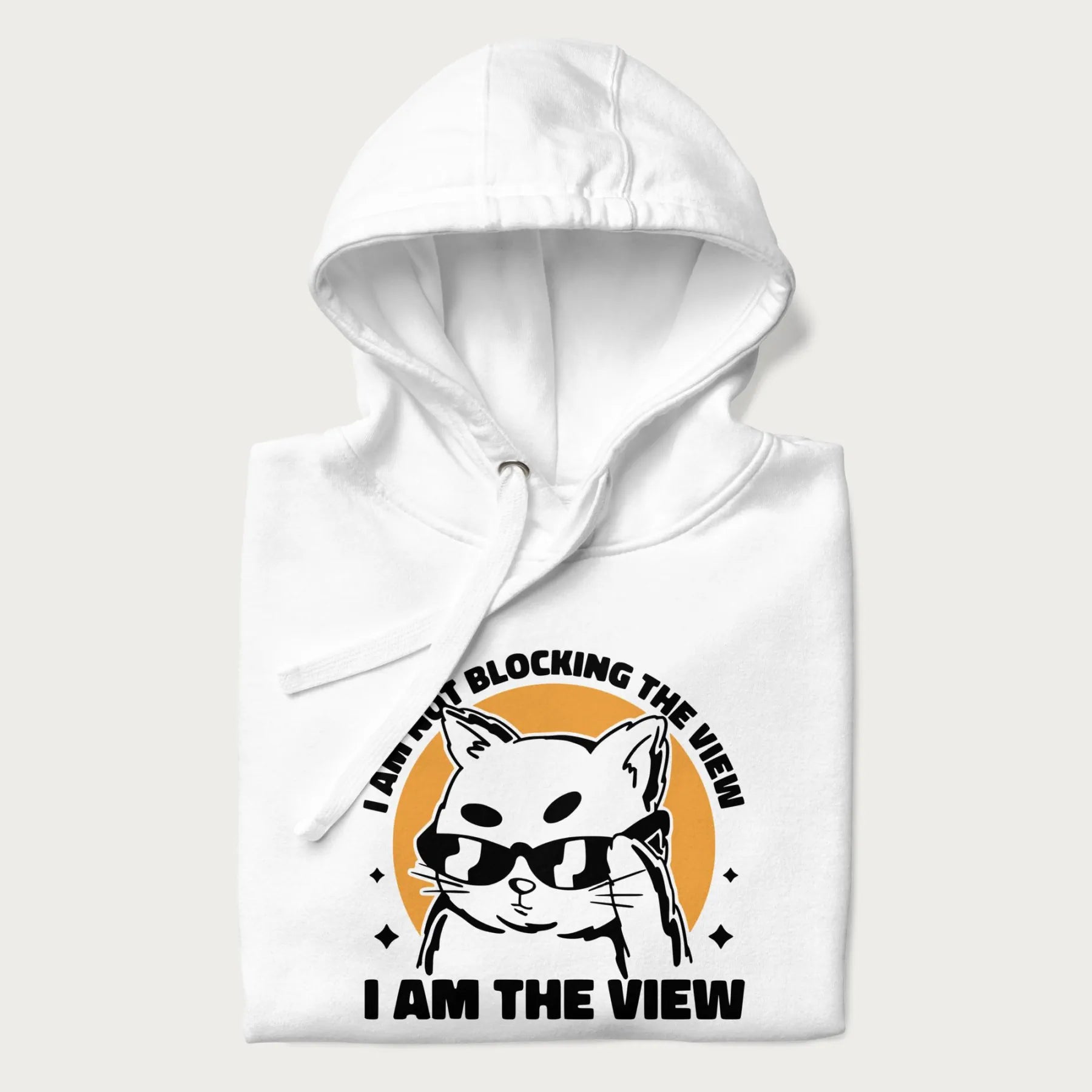 Folded white hoodie with a confident cat wearing sunglasses and the phrase 'I am not blocking the view, I am the view'.