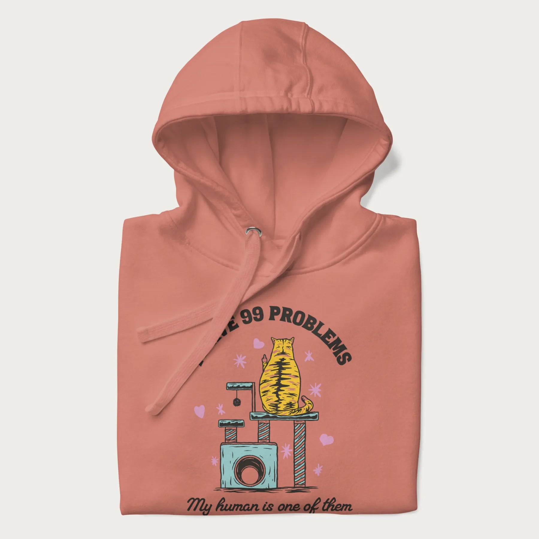 Folded light pink hoodie with graphic of a cat on a scratching post and text 'i have 99 problems, my human is one of them'.