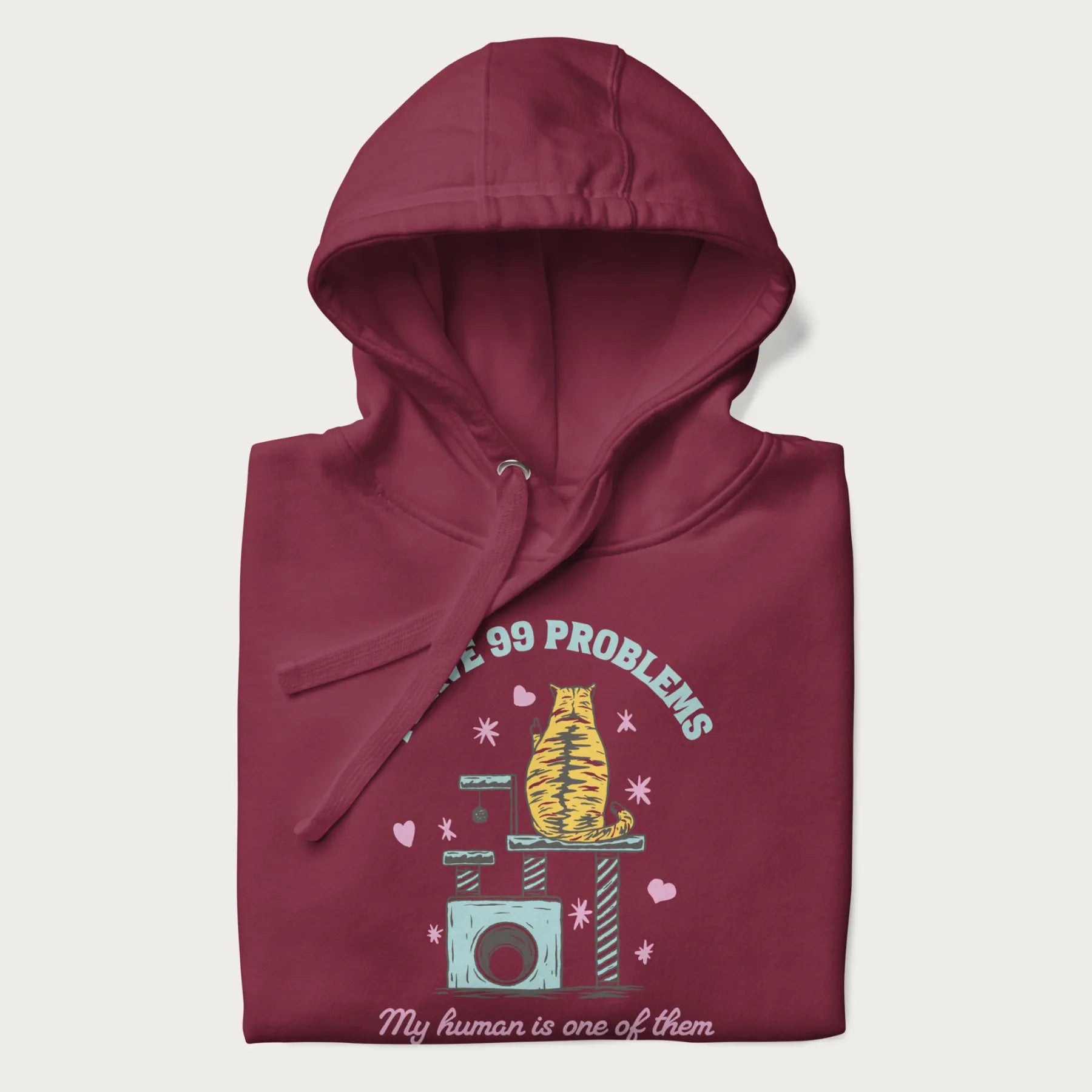 Folded maroon hoodie with graphic of a cat on a scratching post and text 'i have 99 problems, my human is one of them'.