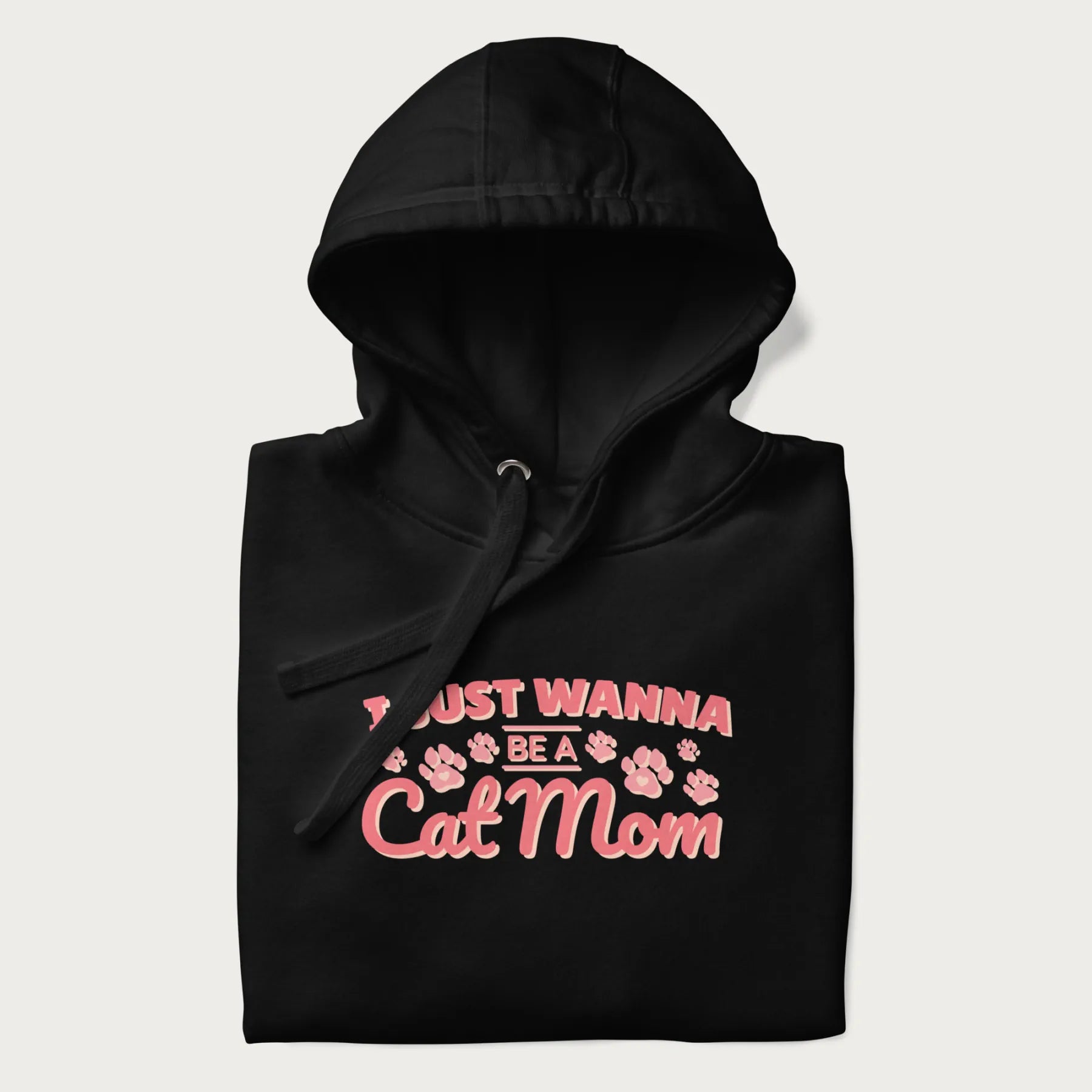 Graphic on a folded black hoodie saying 'I Just Wanna Be a Cat Mom' with pink lettering and paw prints.